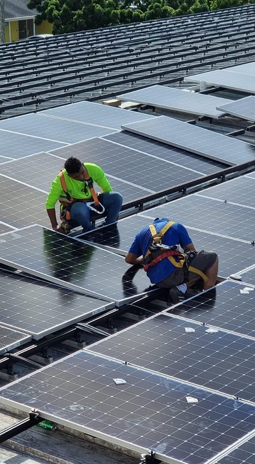 Two GreenTech installers in harnesses fitting panels on a roof